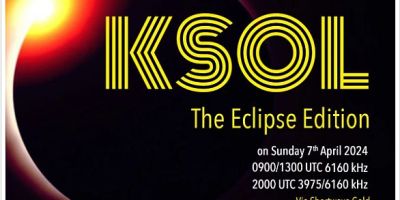 Art work showing, on a blaclk background, a sun of sorts with a white core, a yellow inner ring and a red outer ring, plus a violet bow overlapping its center. Fractured yellow letters letting the black background through, saying "KSOL, The Eclipse Edition", via Shortwave Gold"